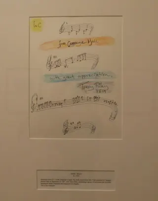 Encadr&eacute;e sur un mur du Carnegie Hall, une page de musique manuscrite de la main de Terry Riley : quelques port&eacute;es de motifs courts, rehauss&eacute;es &agrave; l'aquarelle, portant la d&eacute;dicace &laquo; for Carnegie Hall, with great appreciation &raquo; et sa signature
