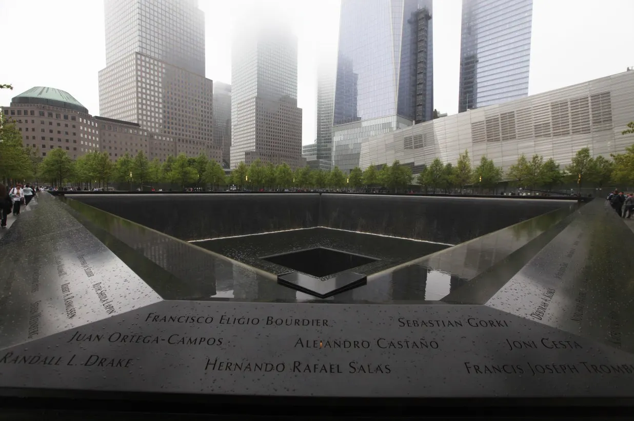 Le parapet de bronze d'un des deux bassins du m&eacute;morial du 11-Septembre, vu de tr&egrave;s pr&egrave;s sous la pluie. Des noms y sont d&eacute;coup&eacute;s en lettres capitales, remplis d'eau : Francisco Eligio Bourdier, Sebastian Gorki, Juan Ortega-Campos, Alejandro Casta&ntilde;o, Joni Cesta, Randall L. Drake, Hernando Rafael Salas. Derri&egrave;re, l'eau tombe dans le vide carr&eacute; du bassin, et plus loin les tours de Manhattan disparaissent dans le brouillard.